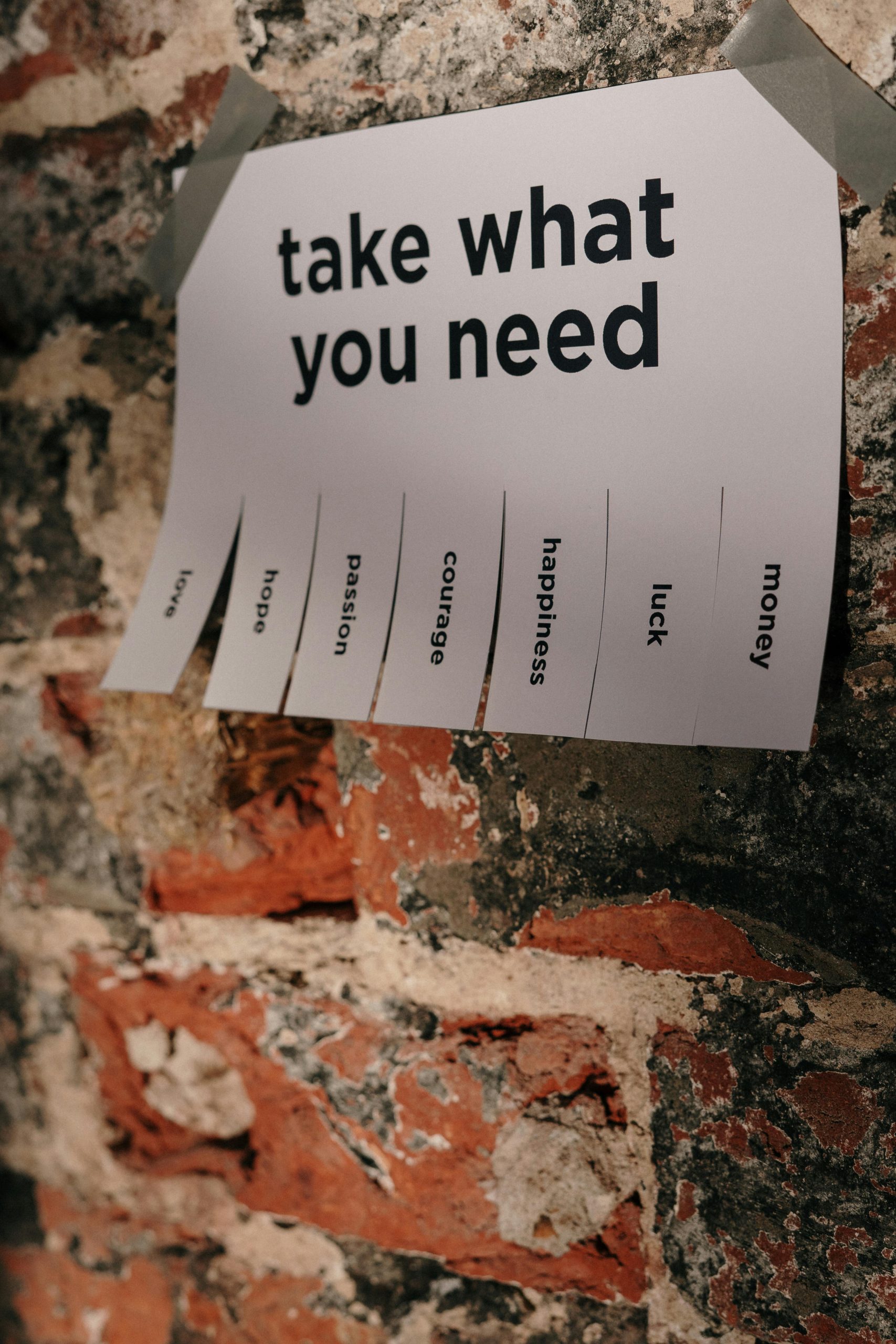 Close-up of motivational poster with tear-off words on a textured brick wall.